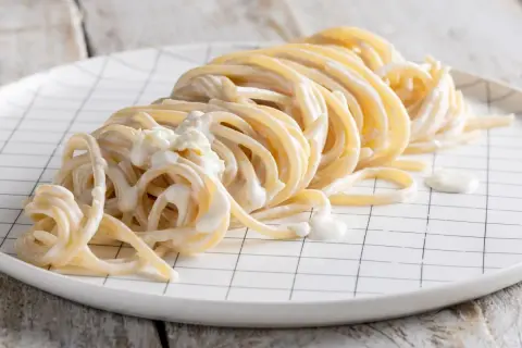 Un piatto di spaghetti avvolti in una cremosa salsa alla panna, serviti su un piatto bianco a quadretti neri.