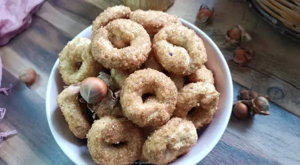 Ciambelline al vino ricetta originale, dorate e croccanti, con nocciole sullo sfondo.