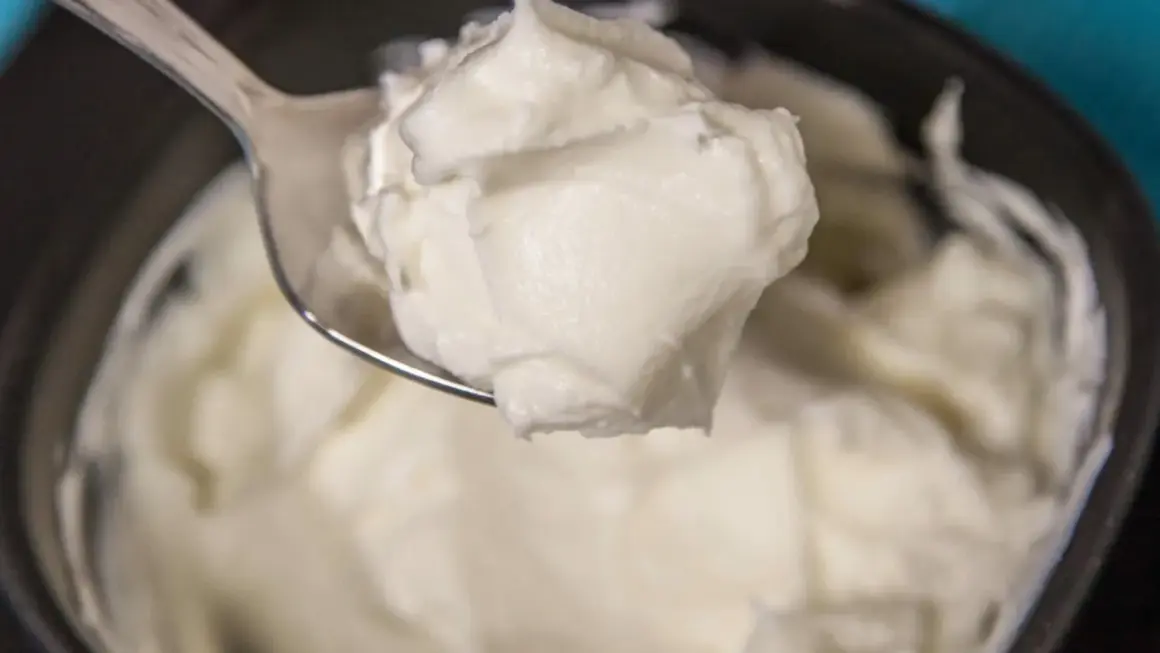 Un cucchiaio raccoglie una generosa porzione di cremoso yogurt greco fatto in casa, pronto per essere gustato.