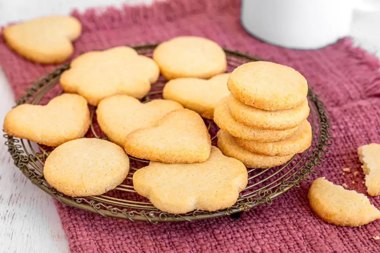 Deliziosi dolci da fare in casa, biscotti a forma di cuore e fiori su un vassoio di metallo, con una tazza bianca sullo sfondo.