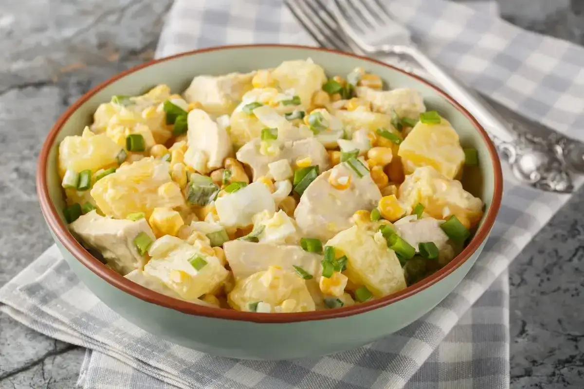 Una ciotola piena di insalata di pollo e patate, con mais, uova sode e cipollotti freschi, condita con una cremosa salsa.