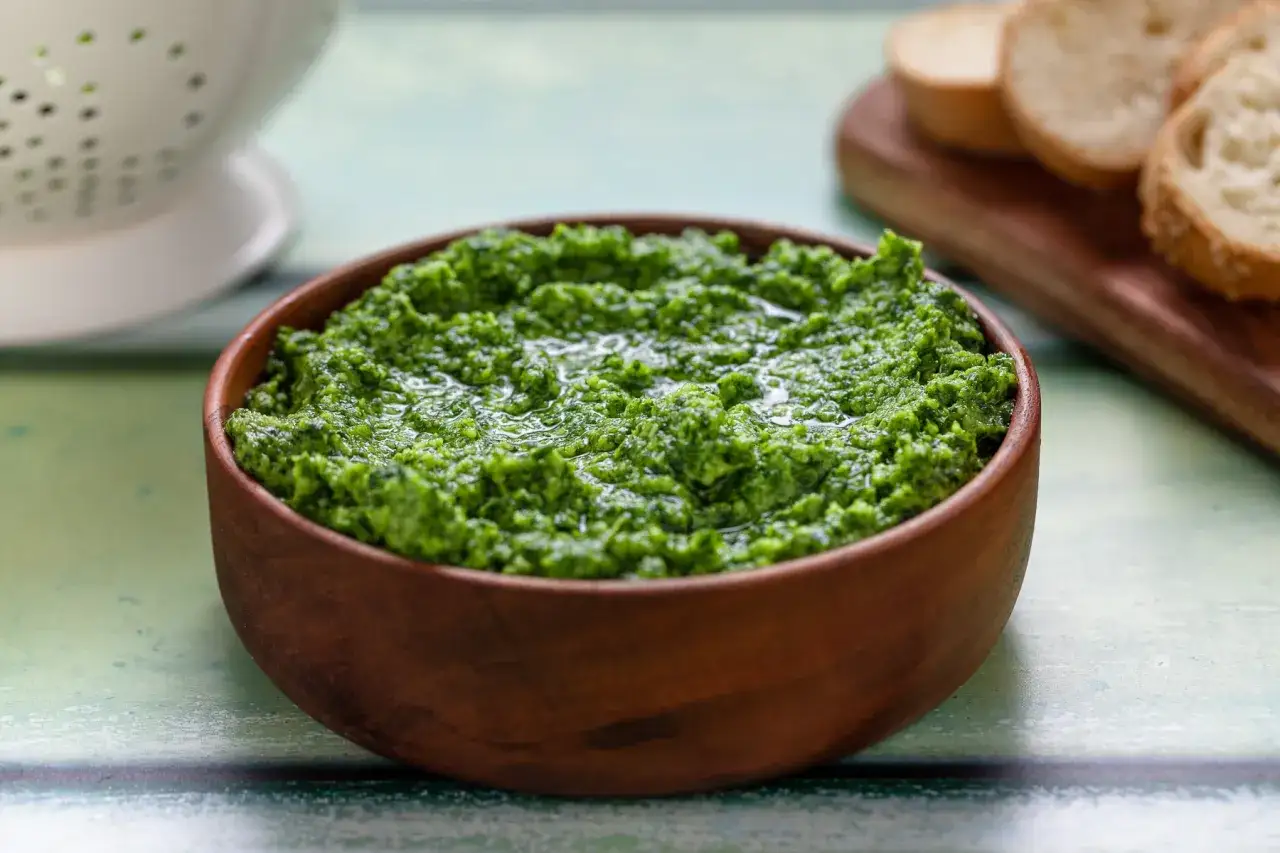 Pesto di rucola Bimby appena preparato, in una ciotola di legno, pronto per essere gustato con crostini.