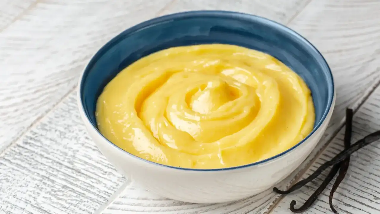 Crema pasticcera ricetta della nonna, densa e vellutata, servita in una ciotola blu con bacche di vaniglia.