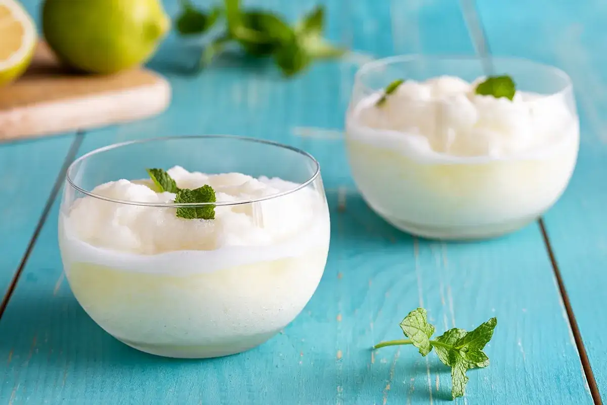 Due coppe di sorbetto al limone fatto in casa, guarnite con menta fresca, su un tavolo di legno blu.