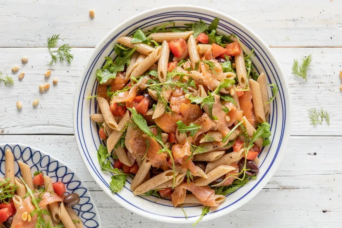 Pasta fredda con salmone affumicato, pomodorini, rucola e pinoli, un piatto estivo fresco e saporito.