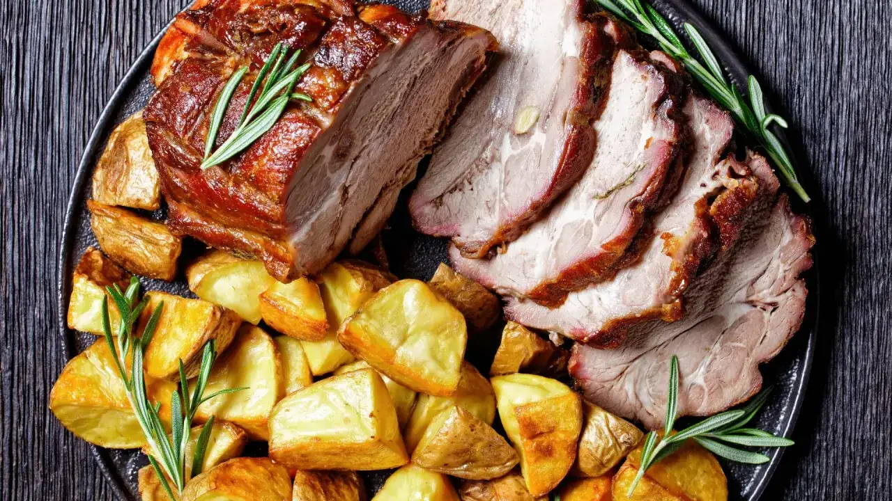 Arista al forno succulenta con patate arrosto dorate e rosmarino fresco su un piatto scuro.