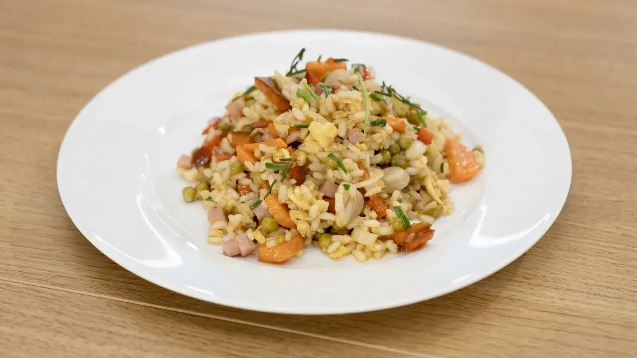 Piatto di riso alla cantonese ricetta originale, con piselli, carote, prosciutto e uovo strapazzato, guarnito con erba cipollina.