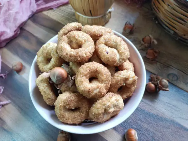 Ciambelline al vino ricetta originale, dorate e croccanti, con nocciole sullo sfondo.