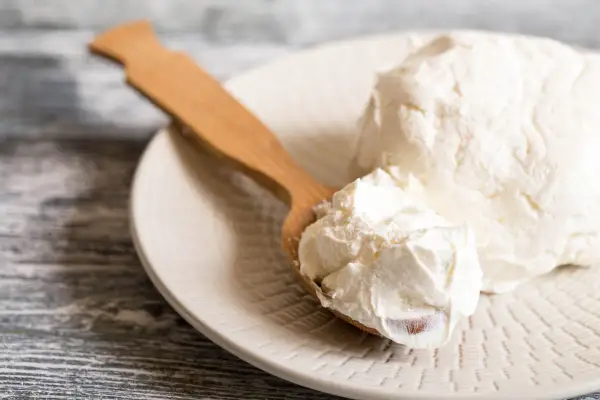 Un cucchiaio di legno raccoglie del cremoso mascarpone da un piatto. Si può congelare il mascarpone per conservarlo più a lungo.