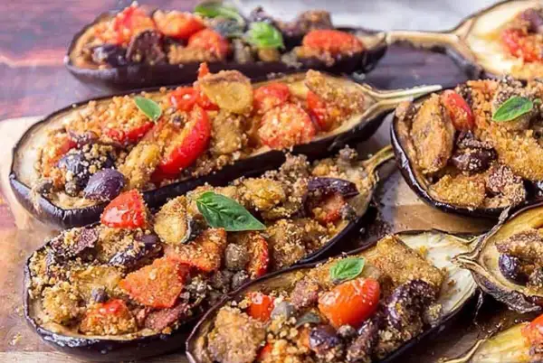 Melanzane a scarpone ripiene di pomodoro, olive e pangrattato, guarnite con basilico fresco. Un piatto saporito e invitante.