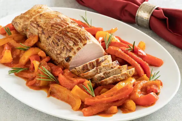 Un arrosto di maiale affettato, servito con peperoni e carote in salsa, un piatto di secondi di carne sfiziosi al forno.
